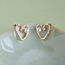 Load image into Gallery viewer, Gold heart-shaped earrings with pearls on a light green surface