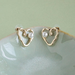 Gold heart-shaped earrings with pearls on a light green surface